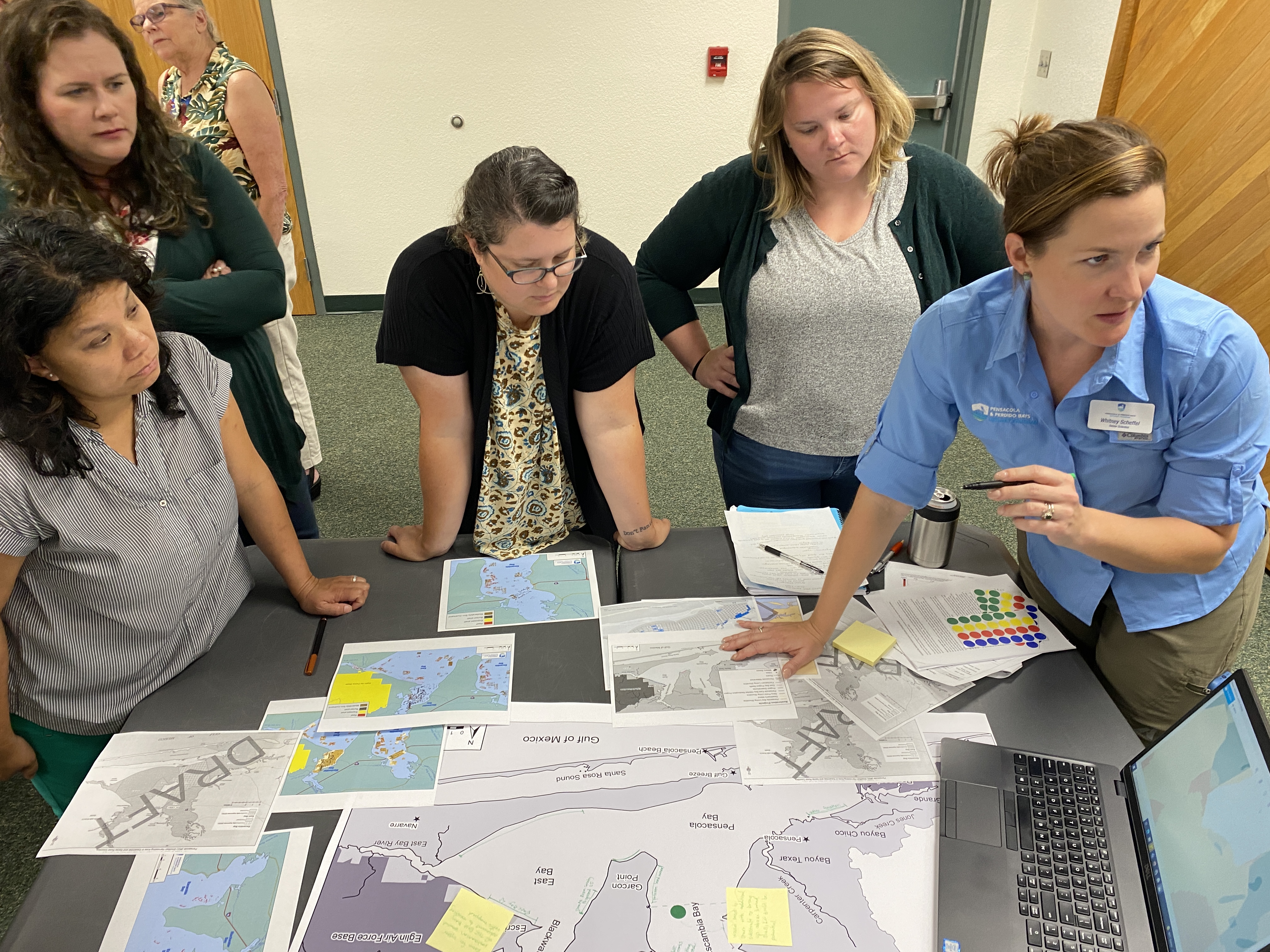 Woman pointing at maps and computer in group of 5 other people models 