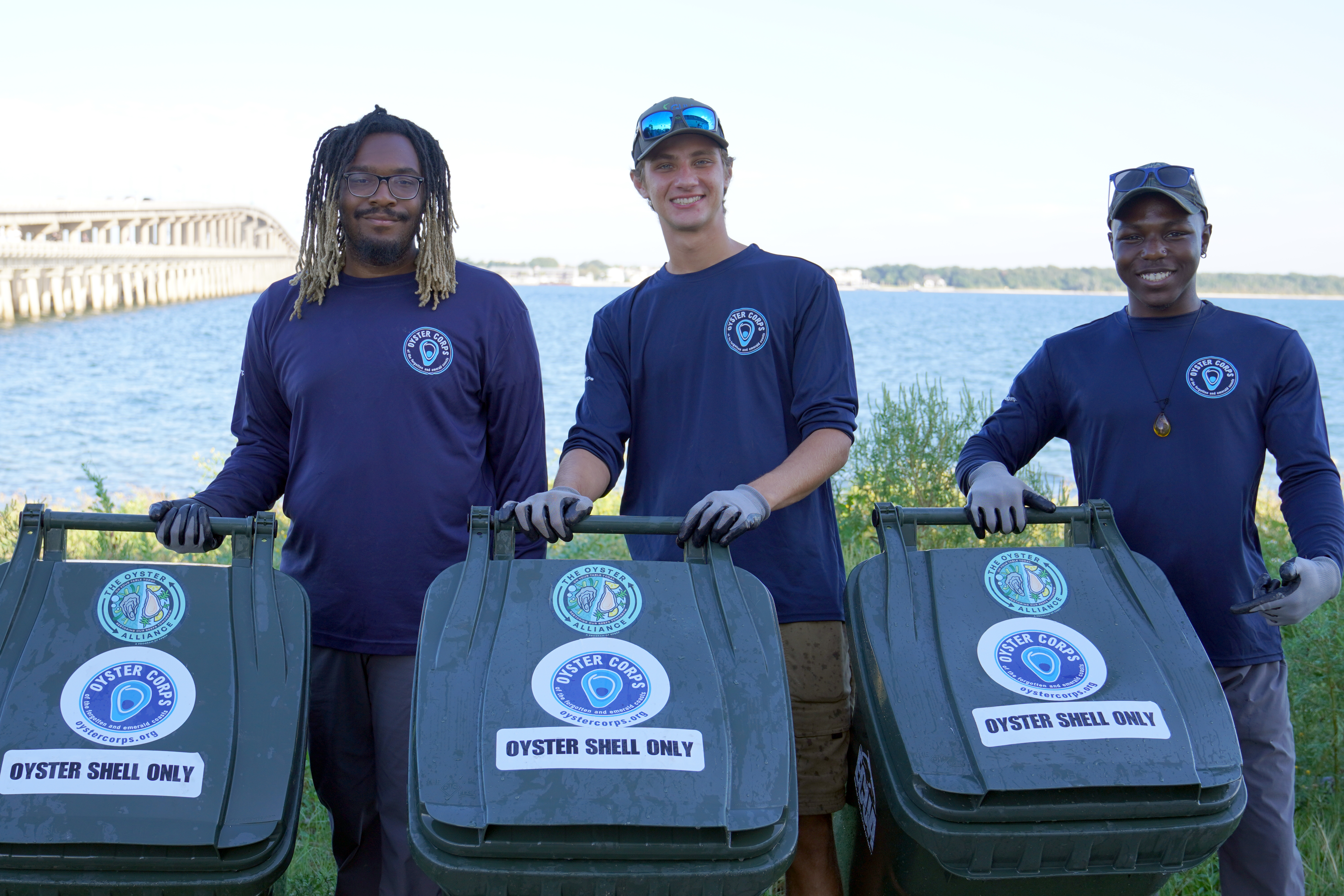 Three Oyster Corps members with shell recycling bins