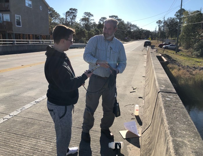 Teacher and student collecting water sample off of bridge