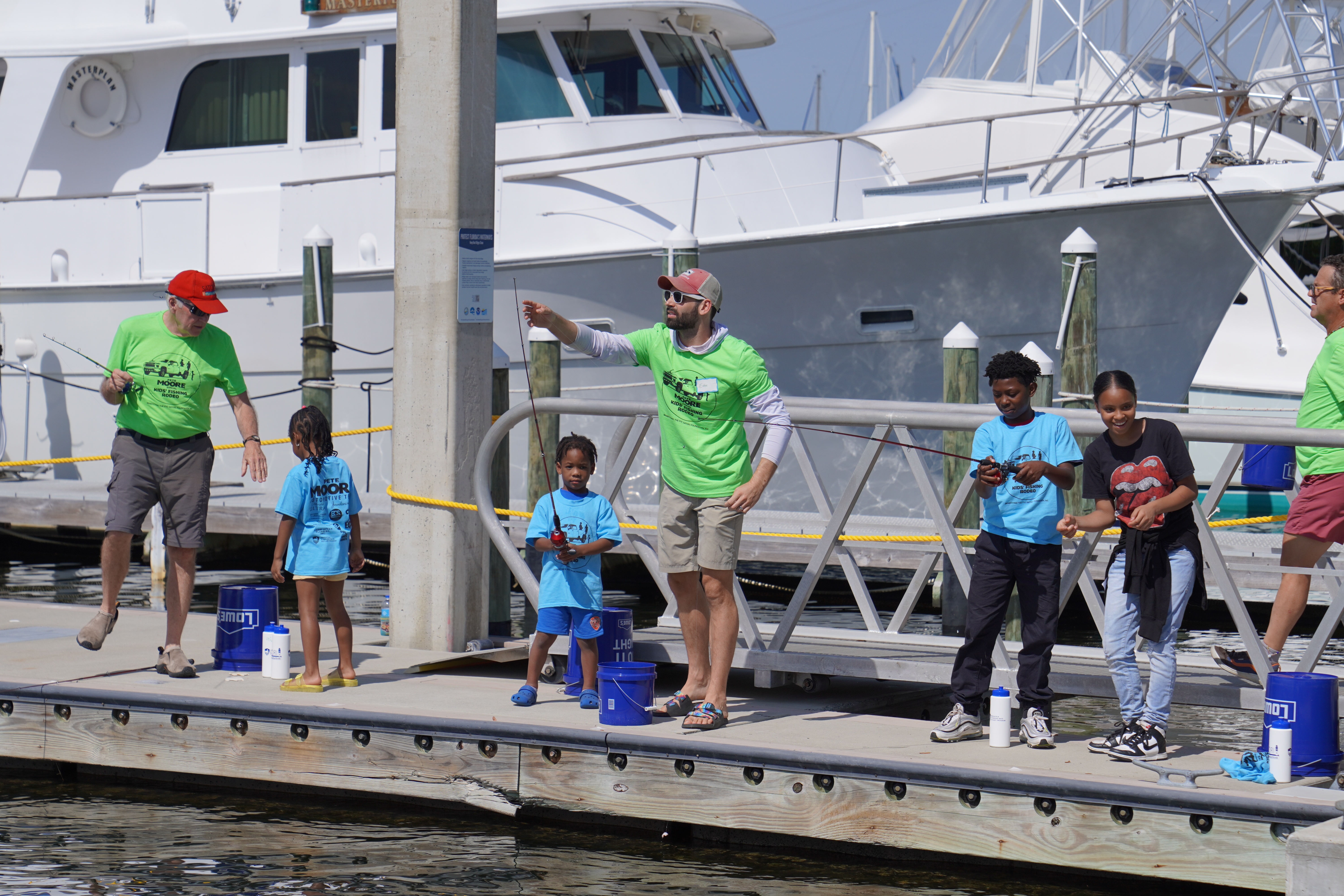 Kids learning to fish with adults instructors from a dock